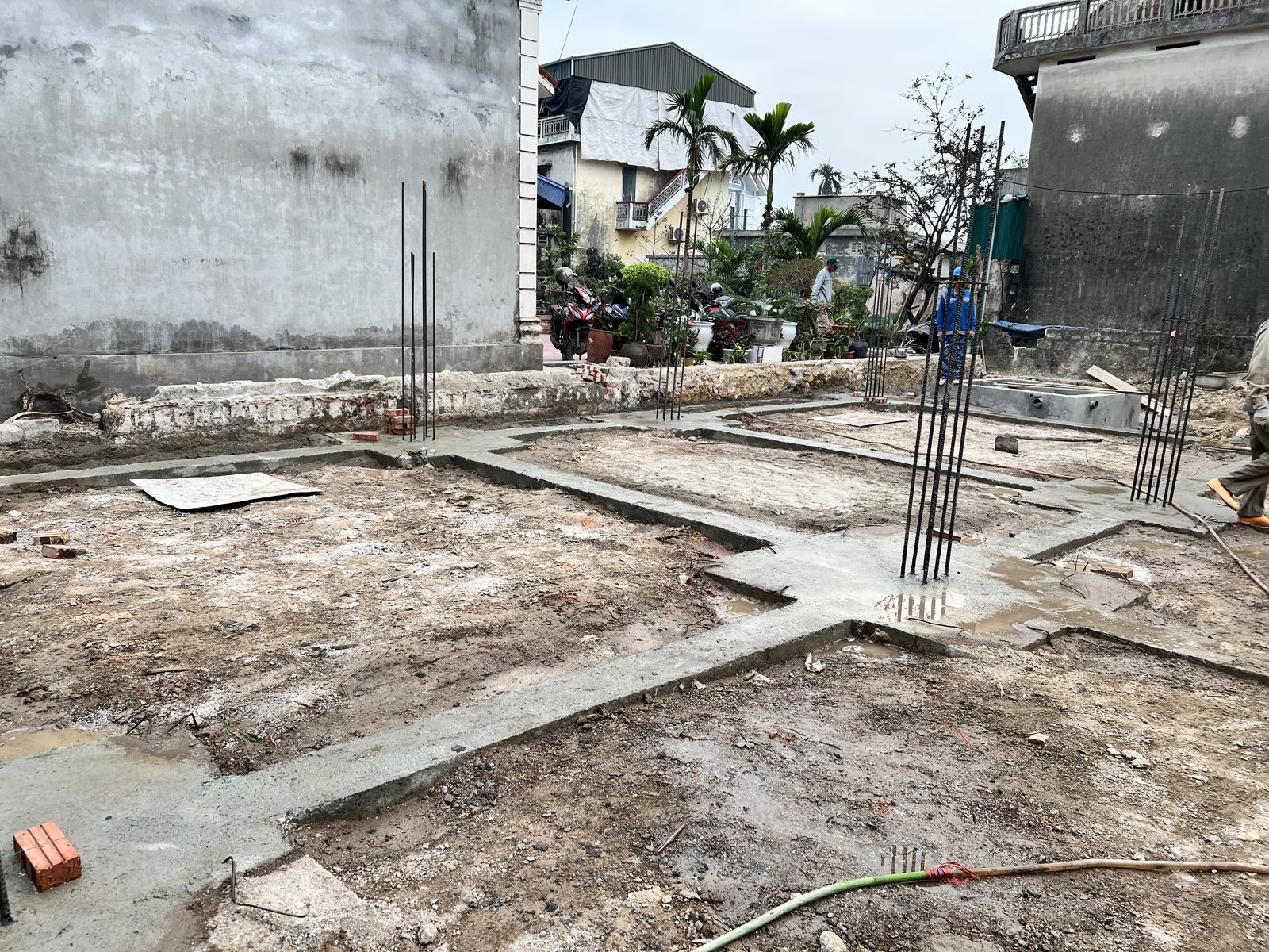 Lớp bê tông lót móng băng nhà dân đổ theo các tuyến, thép chờ cột dựng tại giao điểm, nền đất xung quanh chưa lấp