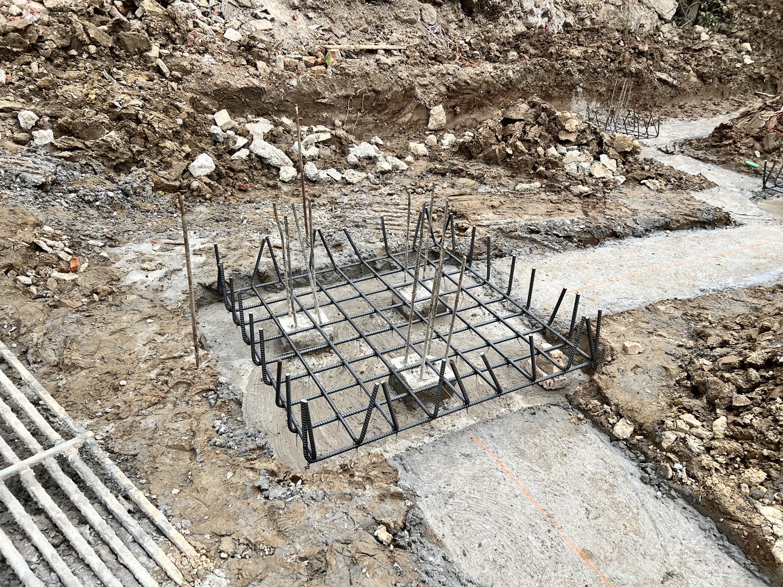 Lưới thép đài móng đã đặt trên lớp bê tông lót, lót rộng hơn lưới thép ở các phía nhìn thấy trong ảnh, thép chờ dựng thẳng