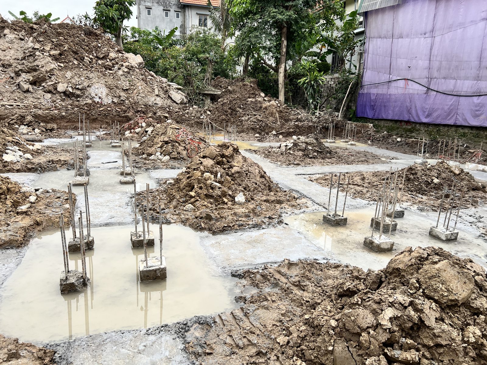 Mặt lót đài móng nhà dân còn đọng nước đục thành vũng quanh các đầu cọc và thép chờ, đất đào chất đống xung quanh