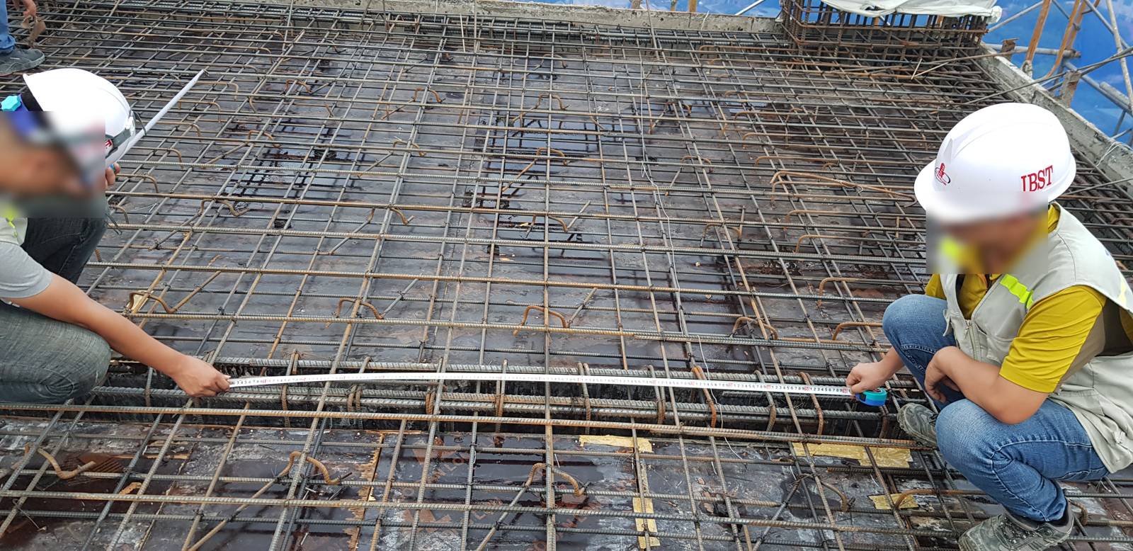 Hai kỹ sư căng thước thép đo khoảng cách lưới thép sàn trước khi đổ bê tông