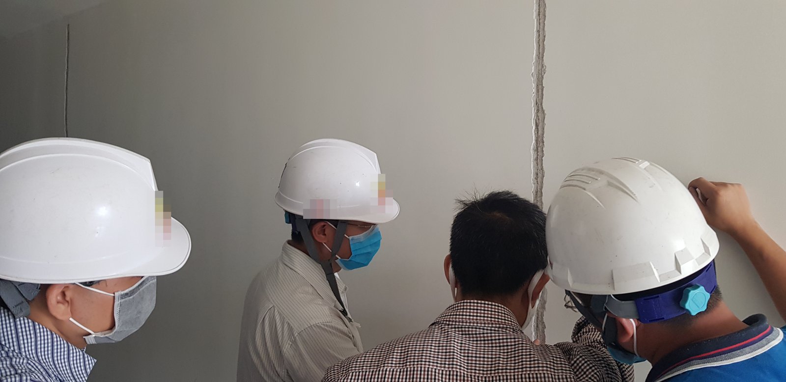 Nhóm kỹ sư đội mũ bảo hộ đứng sát tường, cùng kiểm tra một vị trí tại hiện trường