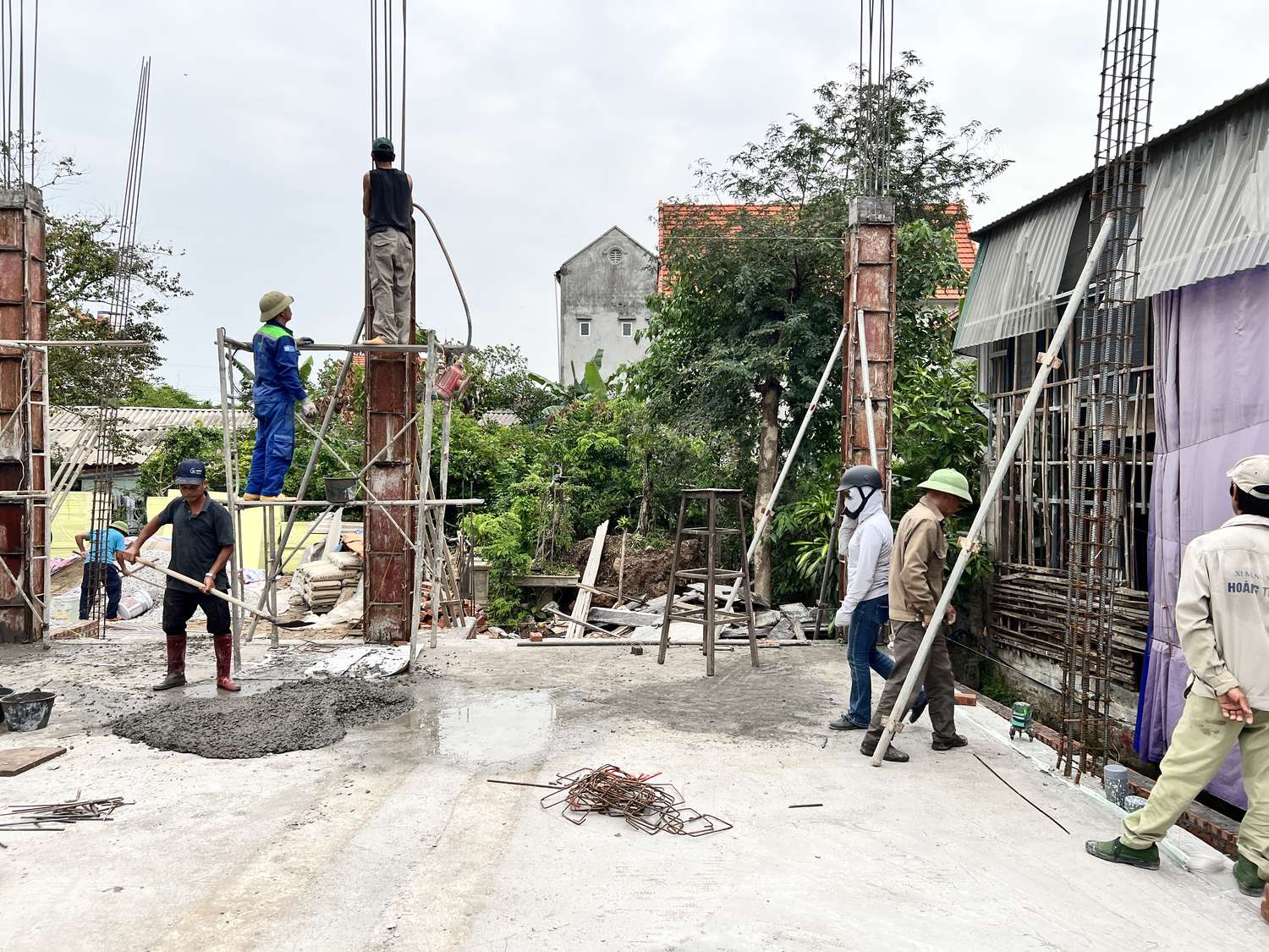 Thợ đang đổ bê tông cột tại công trường nhà dân, cốp pha cột và giàn giáo dựng quanh, nhiều người cùng làm việc