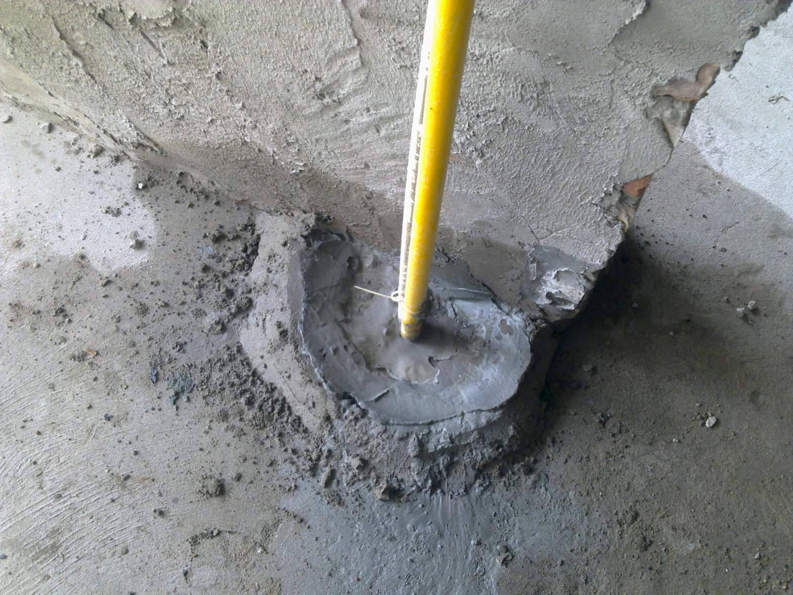 Cổ ống xuyên sàn nhà vệ sinh đã được chèn vữa nhưng bề mặt sàn xung quanh còn vụn vữa và mảnh gạch vỡ