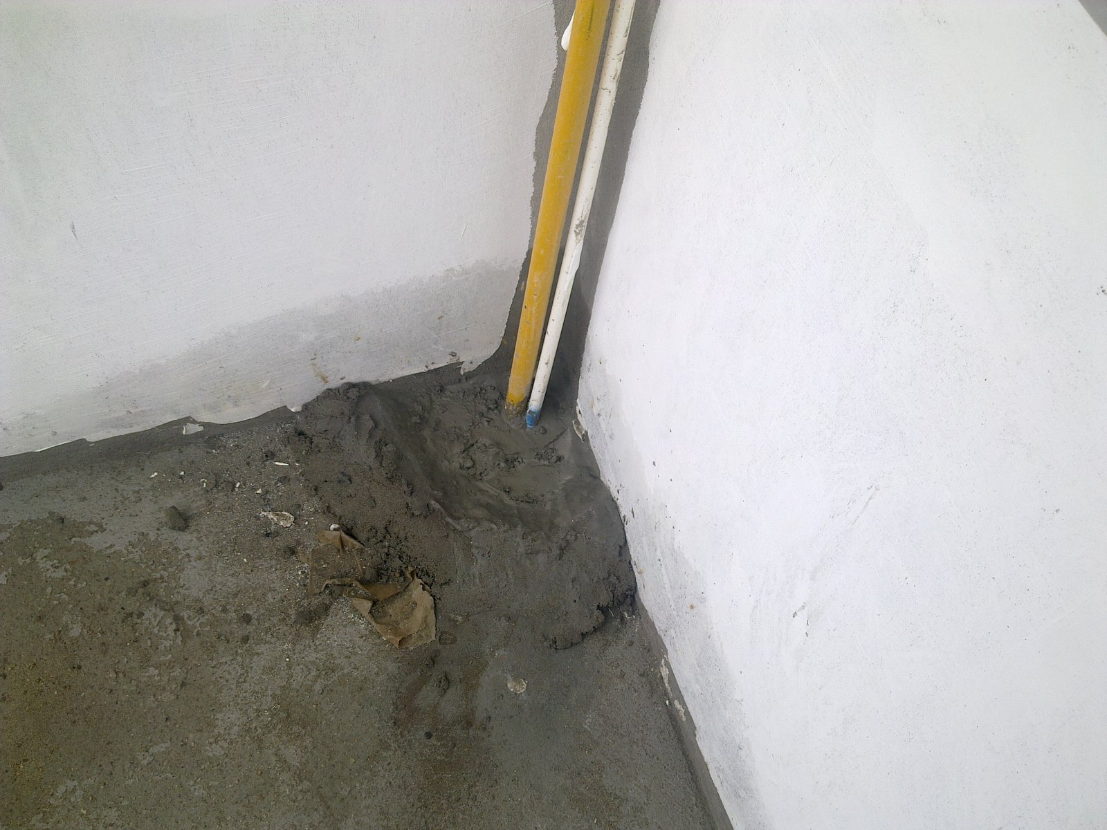 Góc chân tường nhà vệ sinh với ống kỹ thuật xuyên sàn đã chèn vữa, nhưng chân tường vẫn còn là góc vuông chưa bo vát