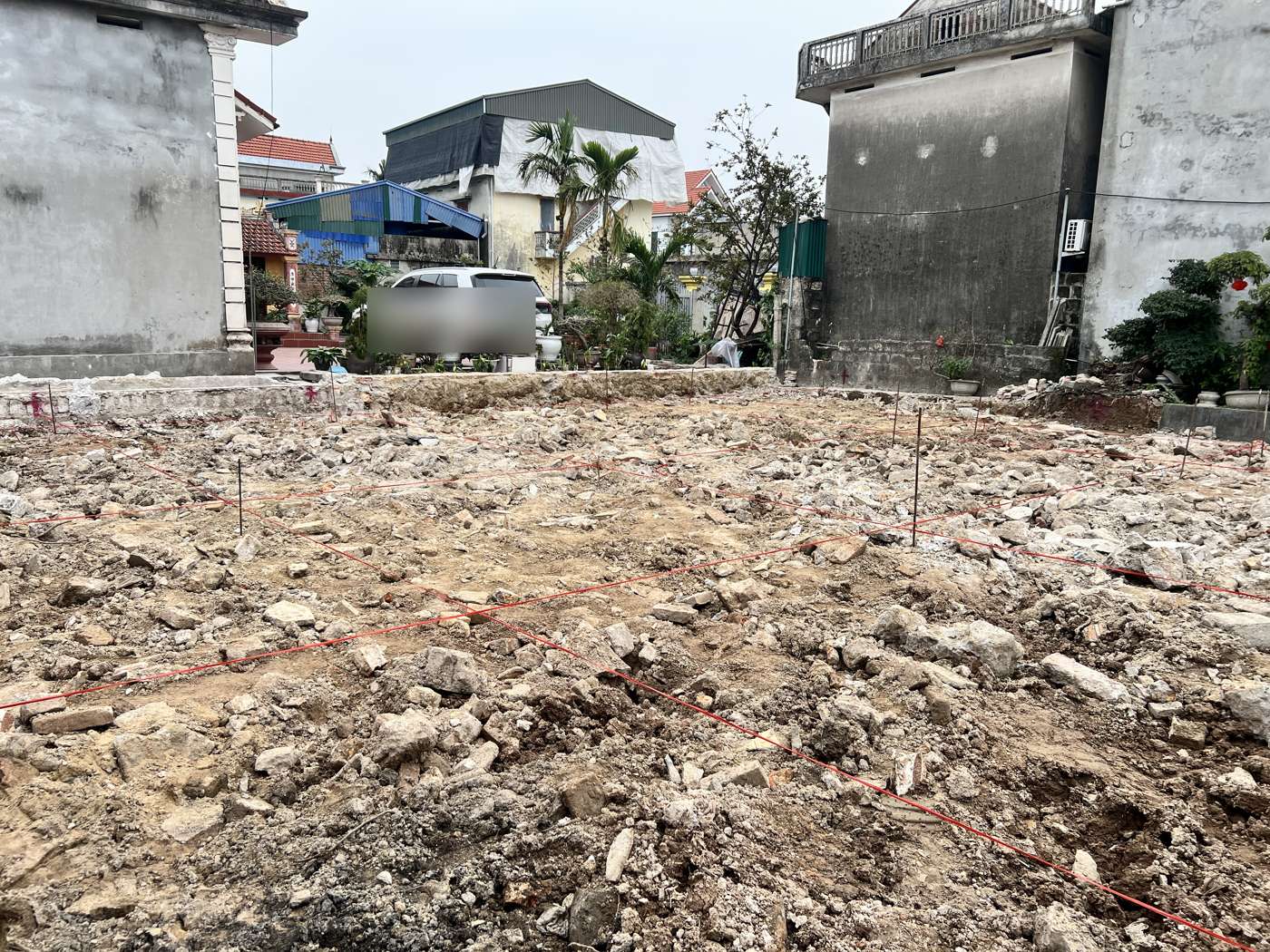 Lưới dây trục màu đỏ căng trên nhiều cọc thép phủ khắp thửa đất vừa dọn mặt bằng, phía sau là tường các nhà liền kề
