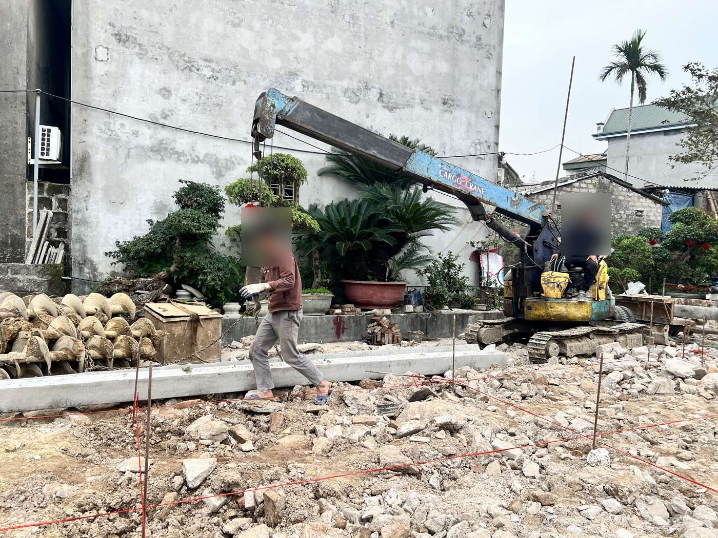 Lưới dây trục đỏ trên cọc thép trải khắp mặt bằng, phía sau là các đoạn cọc bê tông tập kết và máy ép cọc đã vào vị trí