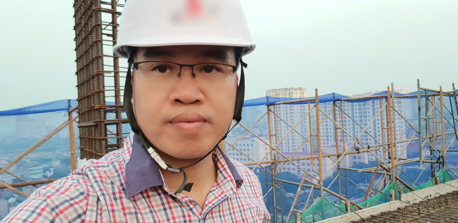 Kỹ sư đội mũ bảo hộ kiểm tra hiện trường tại một công trường đang thi công phần khung, phía sau là cột thép chờ và hệ giàn giáo