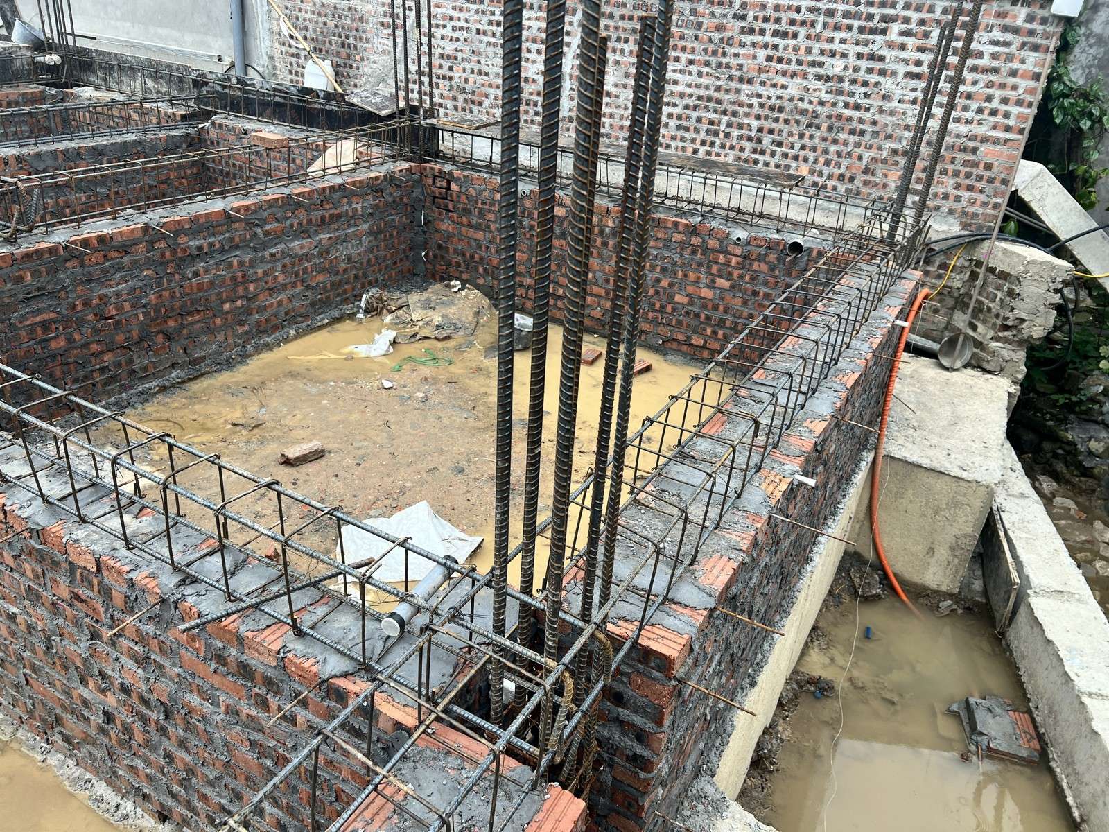 Khe hẹp giữa tường móng mới xây và tường rào công trình bên cạnh đang đọng nước đục, có ống nhựa dẫn xuống