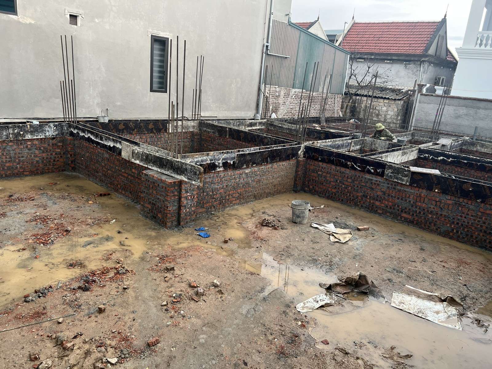 Mặt bằng móng nhà dân, nước đục đọng thành từng vũng trên nền đất giữa các tường móng xây gạch