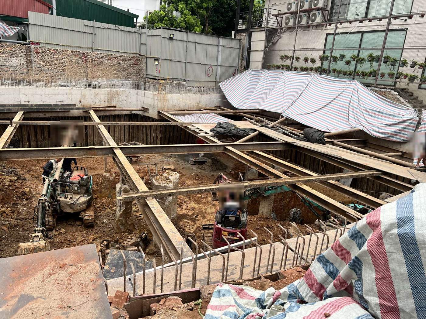 Hố đào rộng có hệ chống vách bằng ván và dầm thép, sát tường của công trình bên cạnh đã được che bạt