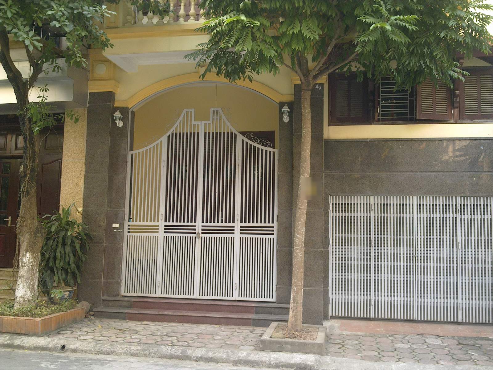 Mặt tiền hai ngôi nhà phố liền kề với cổng sắt, cửa cuốn và vỉa hè lát gạch phía trước