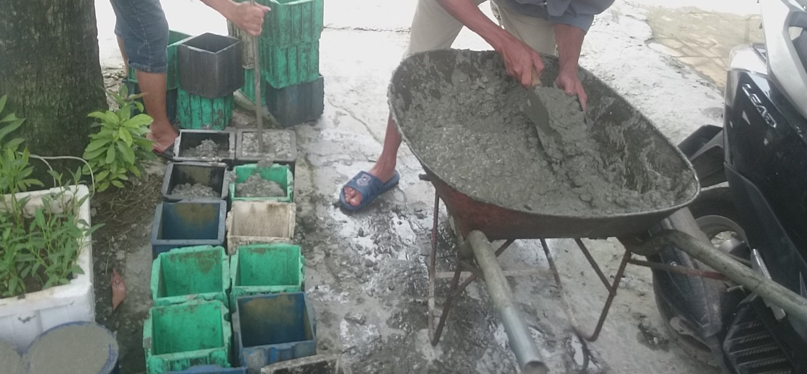 Hai người đang đúc mẫu bê tông vào khuôn lập phương tại công trường, bê tông tươi đựng trong xe rùa