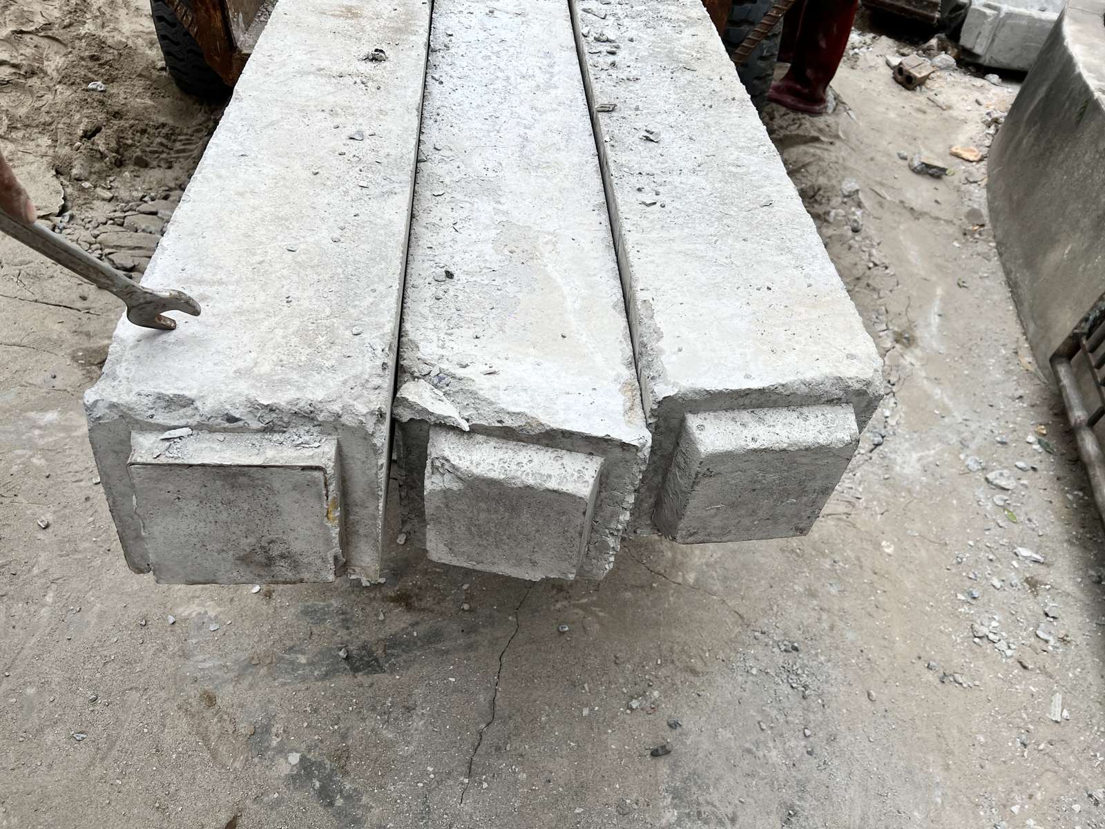 Ba đầu cọc bê tông vuông có vành thép bó đầu, một chiếc cờ lê đặt cạnh, chụp tại công trường trước khi ép