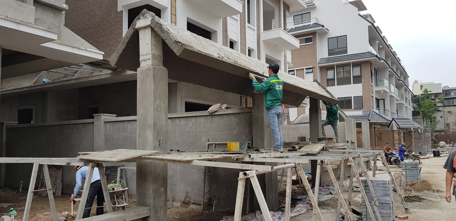 Thợ trát mặt ngoài tầng một của dãy nhà liền kề đang hoàn thiện, đứng trên giàn giáo gỗ