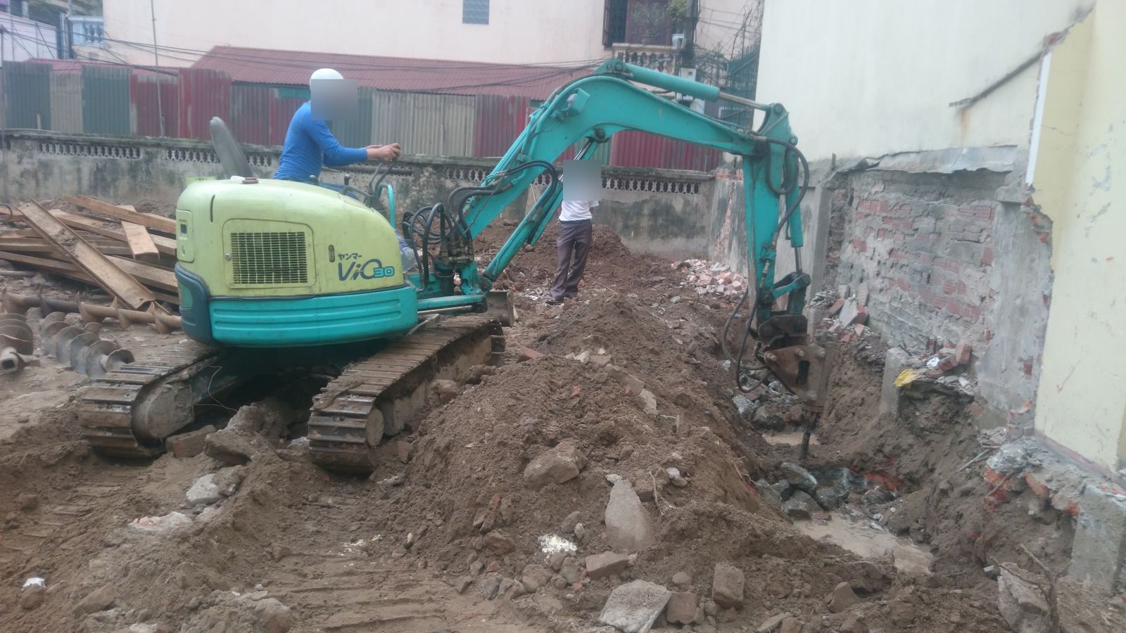 Máy đào mini đang đào hố móng trong ngõ hẹp, sát tường nhà liền kề đã lộ phần chân móng cũ