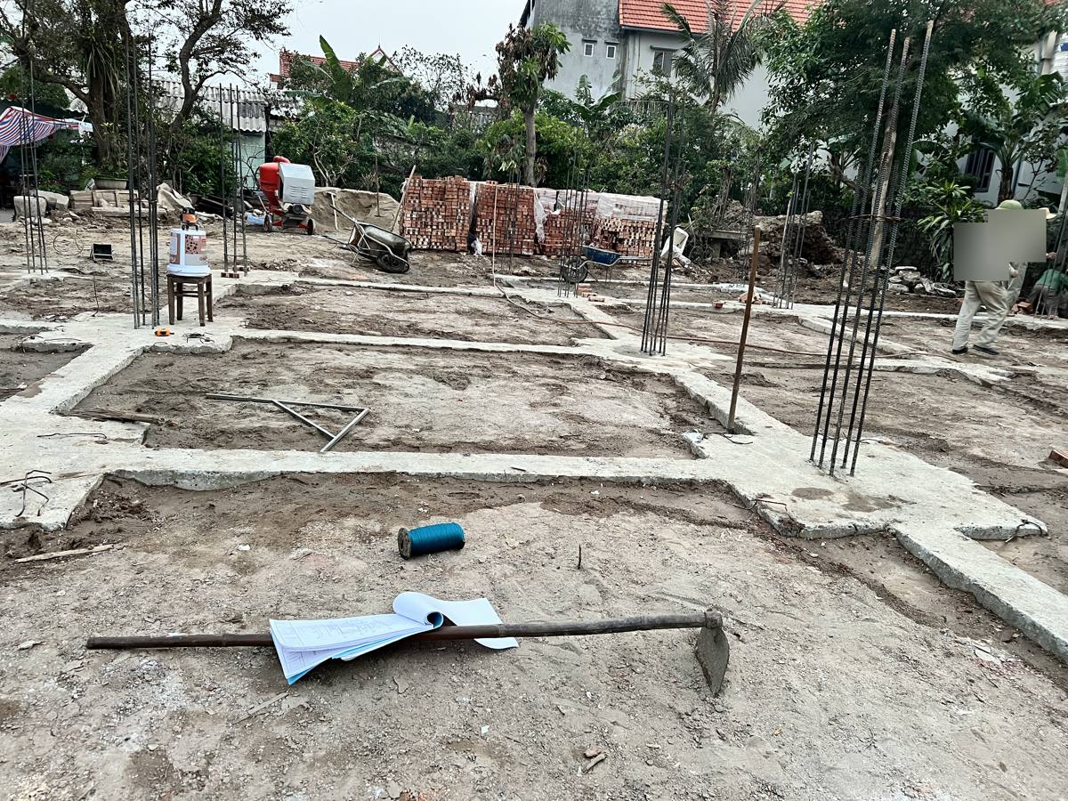 Hệ móng băng nhà dân đã đổ xong lớp bê tông lót, thép chờ cột dựng sẵn, bản vẽ đặt trên nền công trường