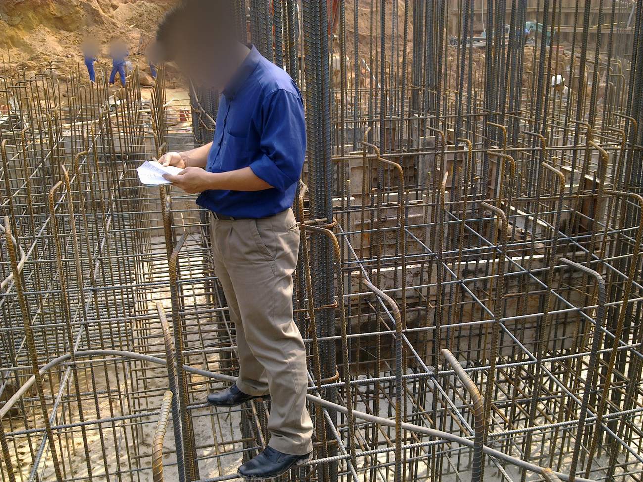 Kỹ sư đứng trên nền cốt thép móng, cầm sổ ghi chép và đối chiếu với bản vẽ trong quá trình nghiệm thu trước khi đổ bê tông