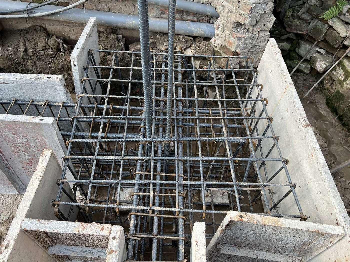 Cận cảnh cốp pha thép định hình của một đài móng nhà dân đặt sát tường nhà liền kề, thép đài đã buộc xong, thép cột chờ dựng lên, khe hở nhìn rõ ở các góc ghép