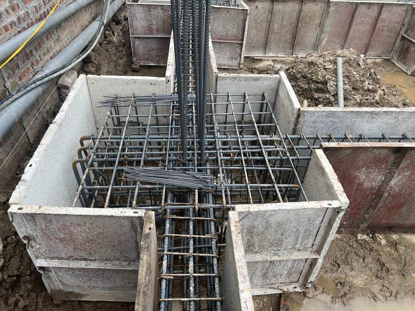 Góc ghép cốp pha đài móng có khe hở rõ ở chân tấm, một bó thép thừa và các mẩu thép rời nằm trong lòng khuôn chưa được dọn