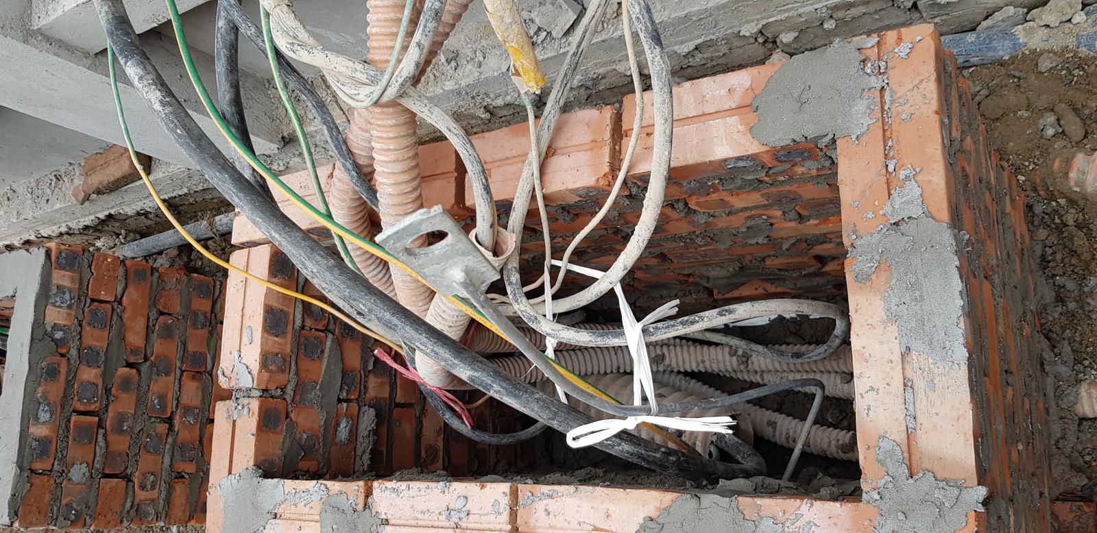 Nhiều tuyến dây điện và ống luồn chui lộn xộn qua một lỗ chờ trên tường gạch, các đầu dây chỉ được bó tạm bằng dây rút