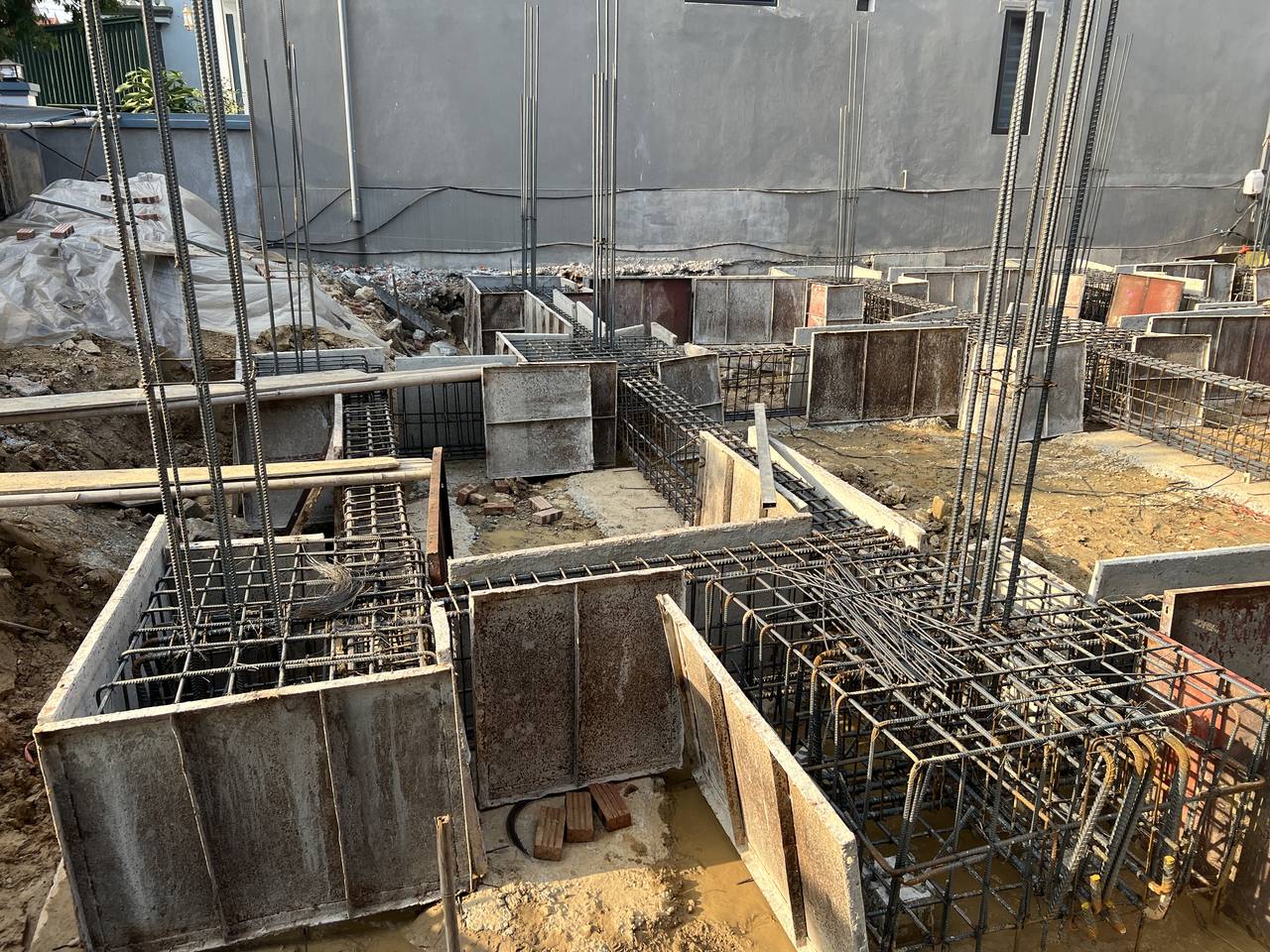 Lòng cốp pha đài và giằng móng còn nước đọng và mẩu gạch vụn ở đáy, thép chờ cột dựng sẵn