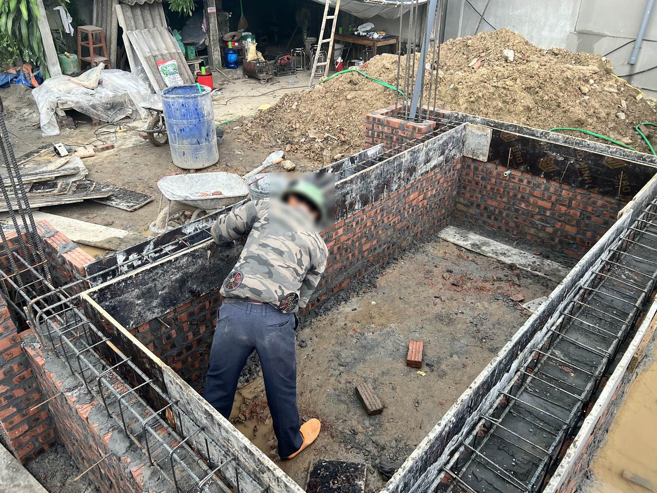 Lồng thép giằng móng đặt trong ván khuôn trên tường móng xây gạch, thép dọc và thép đai nhìn rõ từ trên xuống