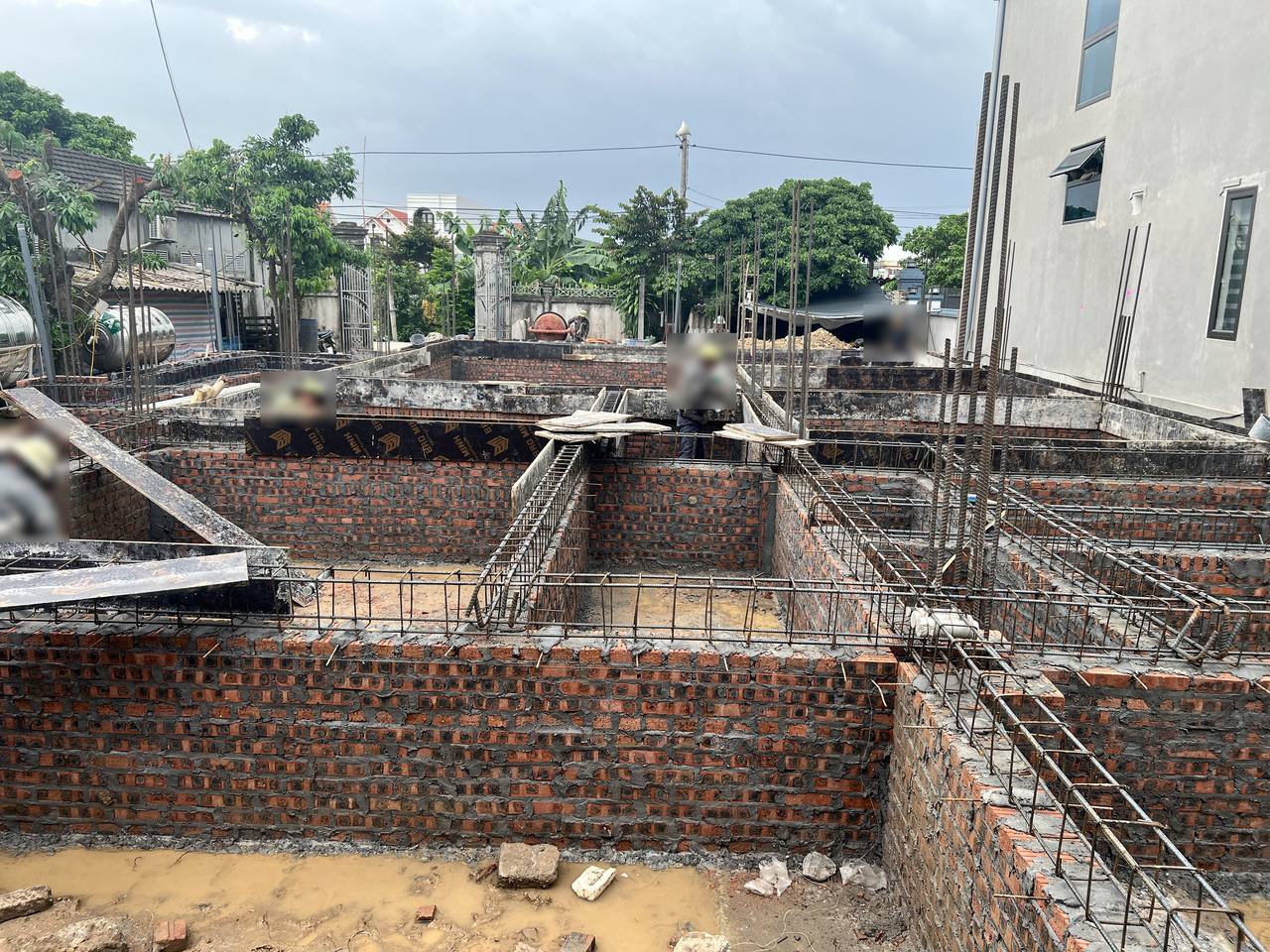 Lồng thép giằng móng đặt trên đỉnh tường móng xây gạch, phía sau đã dựng ván khuôn hai bên giằng