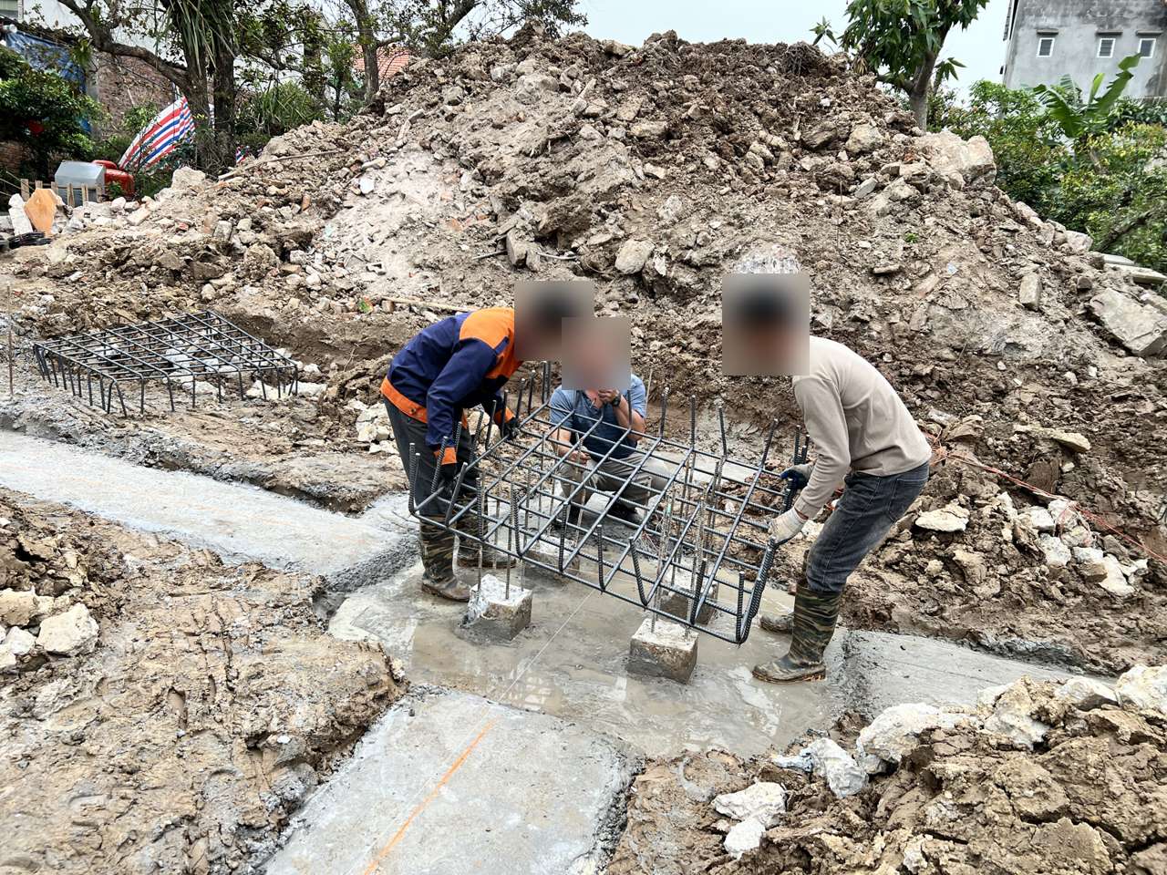 Ba người hạ lưới thép đài cọc xuống hố đài, các đầu cọc có thép lộ ra nằm trong phạm vi lưới