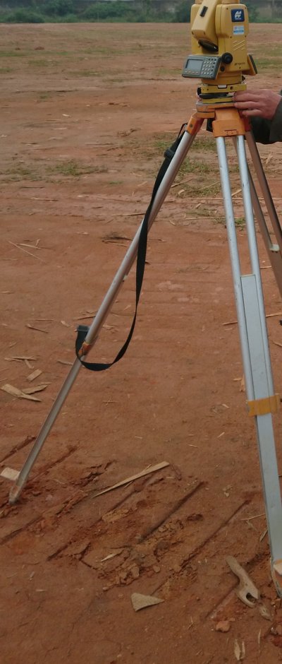 Máy trắc đạc màu vàng đặt trên chân ba càng tại công trường, bàn tay người đang thao tác máy