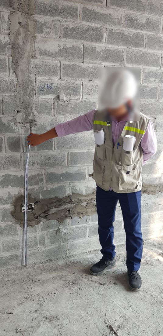 Kỹ sư dùng thước đo kiểm tra một tuyến rãnh đã trát vá trên tường xây tại công trường