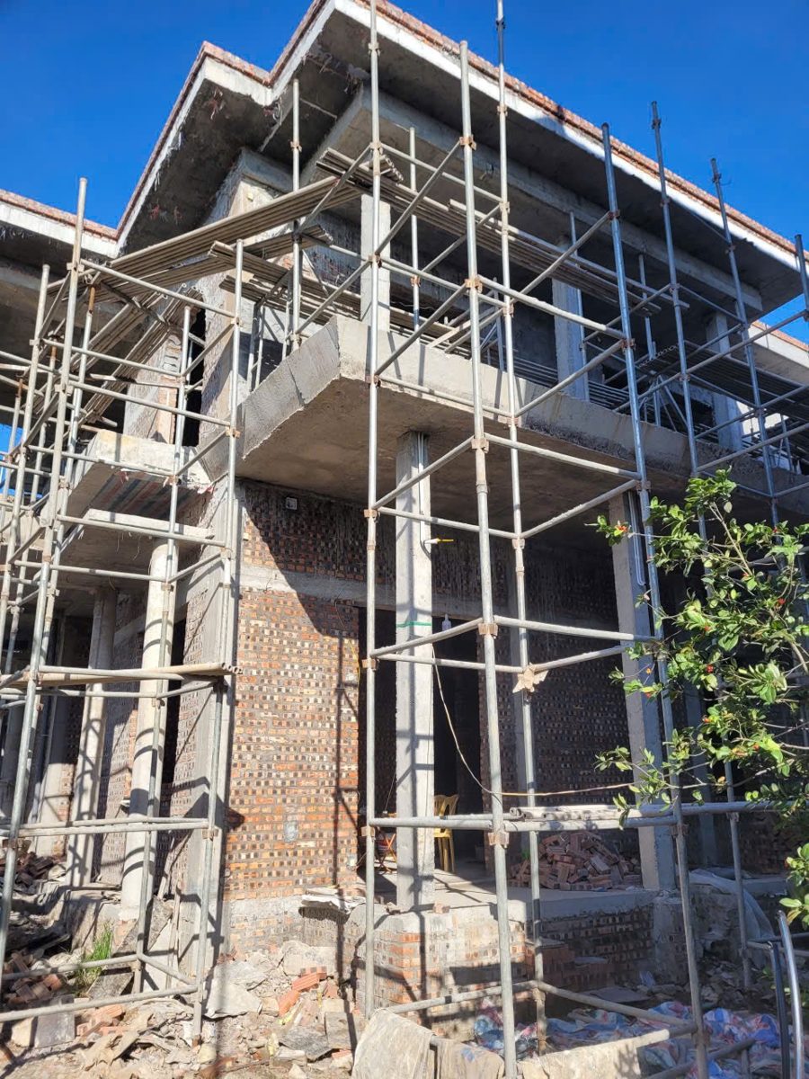 Nhà ở riêng lẻ đang xây, tường gạch chèn giữa hệ cột và dầm bê tông cốt thép, giàn giáo còn dựng quanh nhà