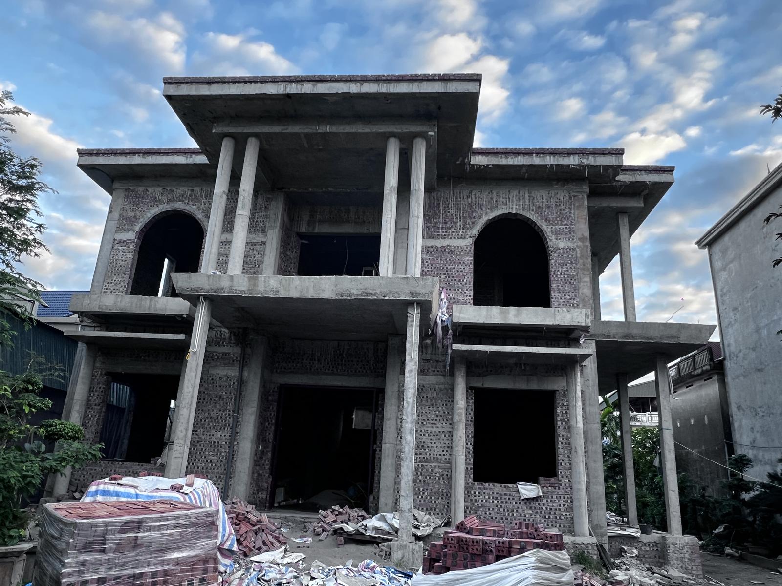 Công trình nhà ở riêng lẻ hai tầng đang xây thô, gạch và vật tư tập kết trước nhà