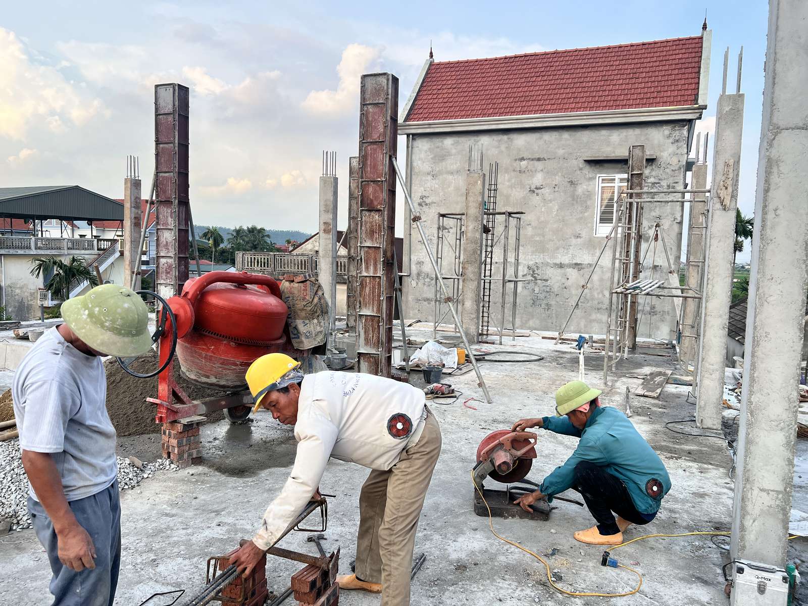 Công trường xây nhà dân với thợ đang gia công cốt thép, cốp pha cột và máy trộn bê tông