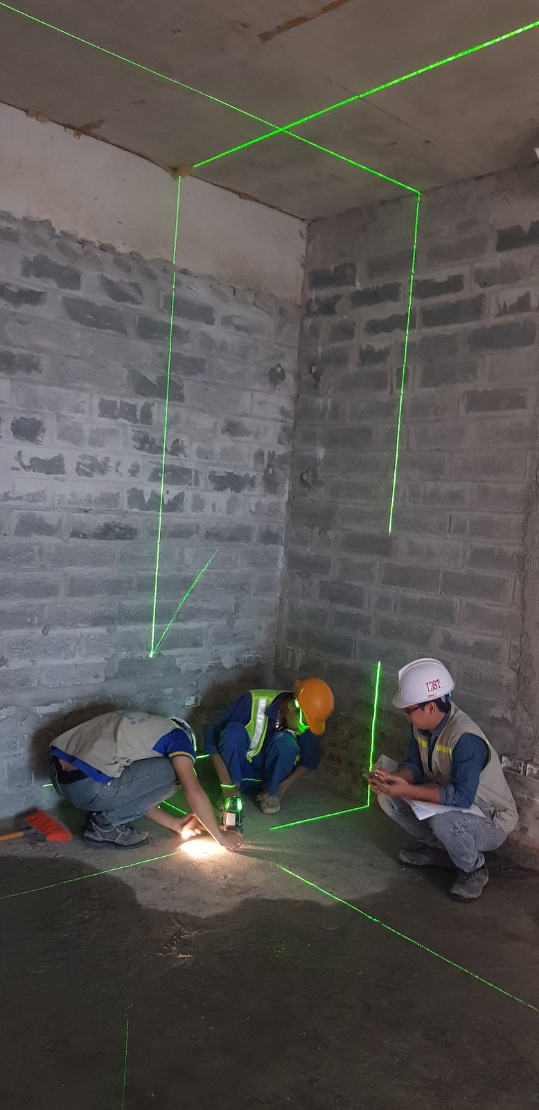 Ba kỹ sư kiểm tra cao độ và vị trí bằng máy laser trong phòng, một người ghi chép vào sổ
