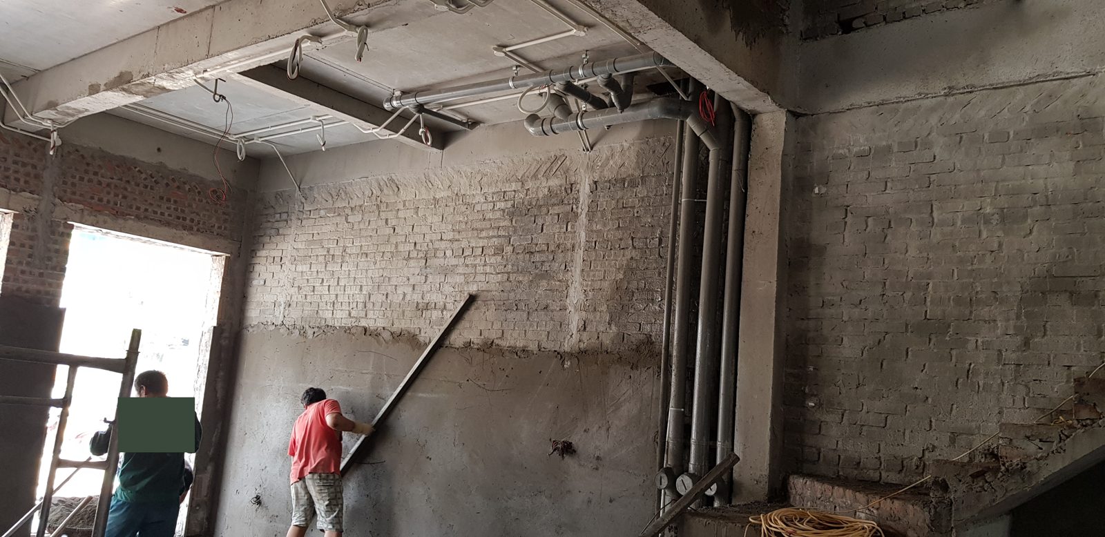 Thợ dùng thước tầm cán phẳng lớp trát theo dải mốc vữa đã đắp sẵn trên tường