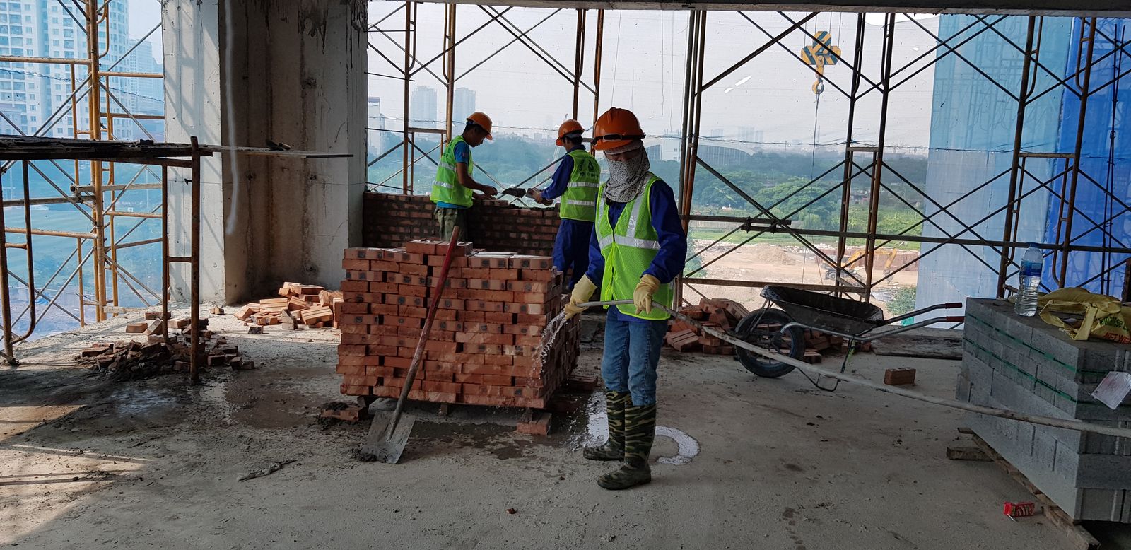 Thợ xây tường gạch trên công trường, một người đang tưới ẩm chồng gạch trước khi đưa vào xây