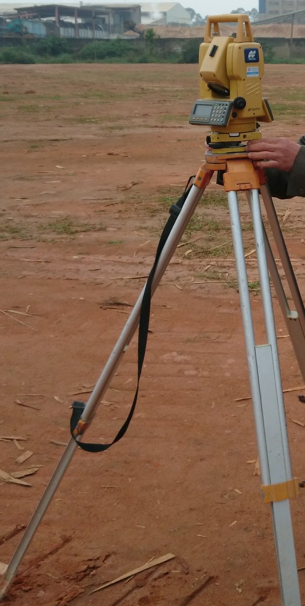 Máy trắc đạc màu vàng đặt trên chân ba càng tại công trường, bàn tay người đang thao tác máy