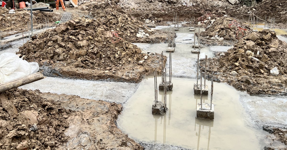 Nước đục đọng thành vũng trên lớp lót hố đài, ngập quanh chân các đầu cọc có thép lộ ra